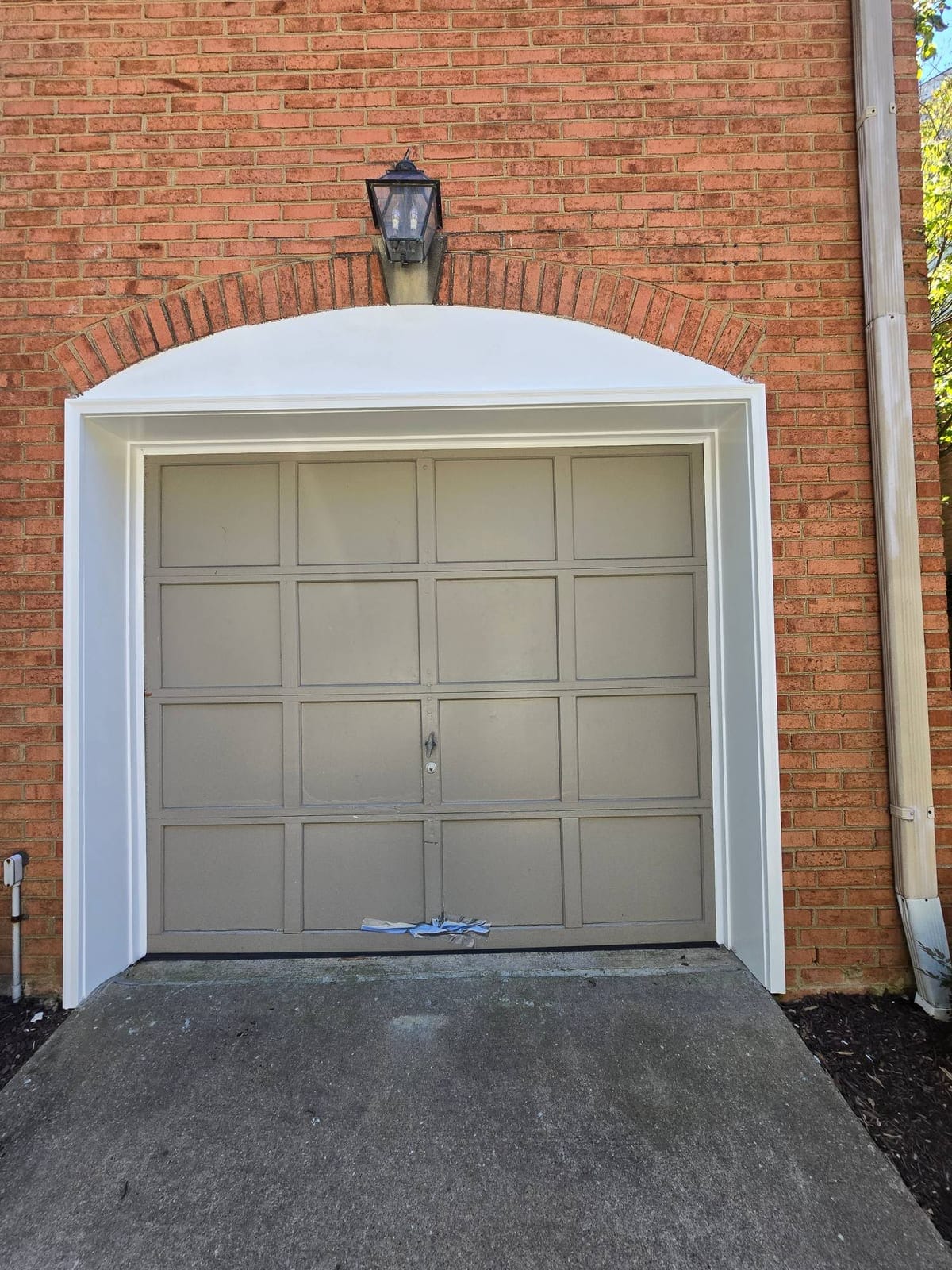 Painted panel garage door under a brick arch on a Rockville home, with a strip of torn weather seal hanging along the bottom edge