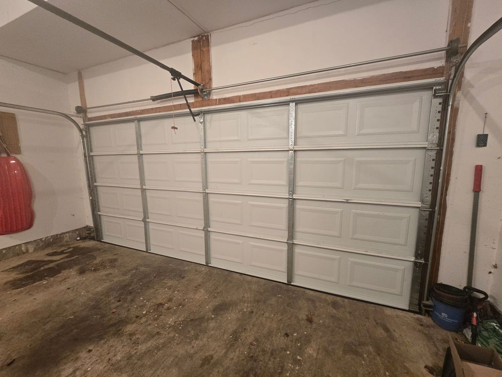 Inside view of a white steel garage door with the torsion shaft, cable drums, track, and opener arm visible above it